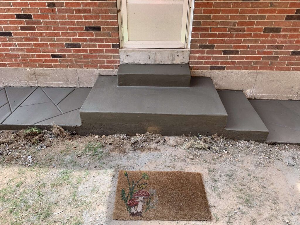 A brick building with concrete steps and a welcome mat in front of it.