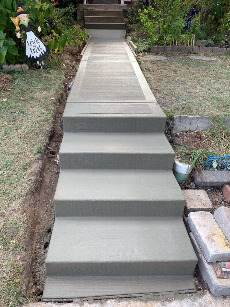 A concrete walkway with stairs leading up to a house.