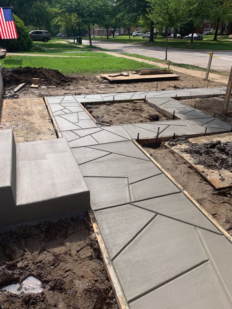 A concrete walkway is being built in front of a house with an american flag in the background.