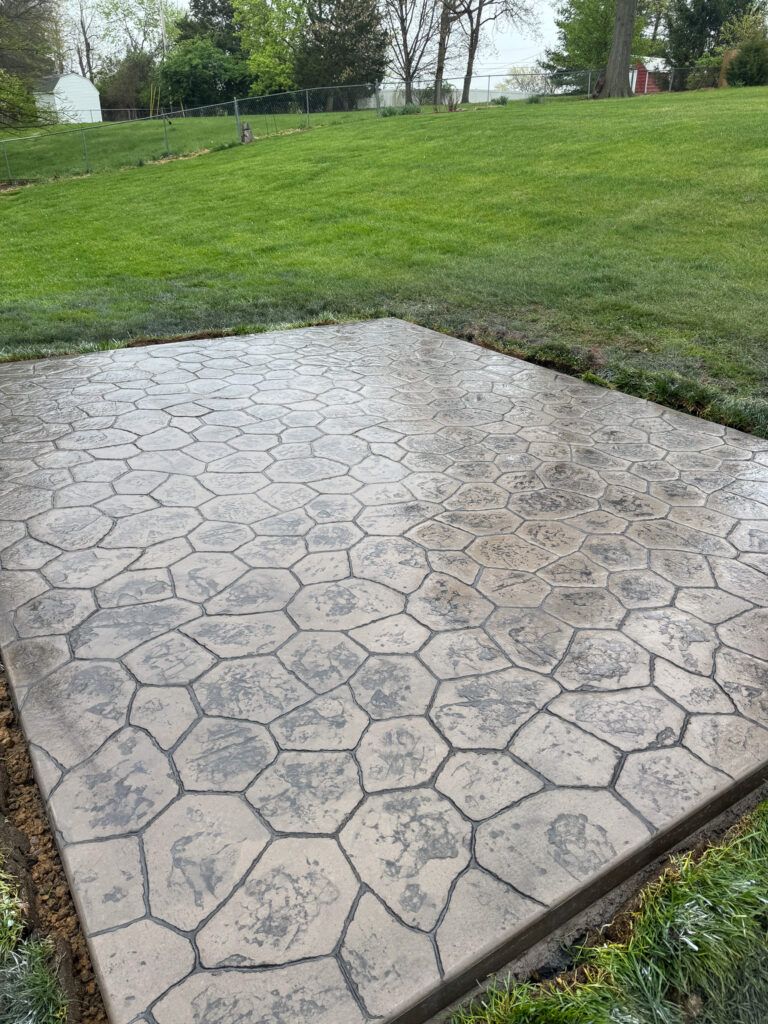 A concrete patio with a pattern on it is in the middle of a lush green field.