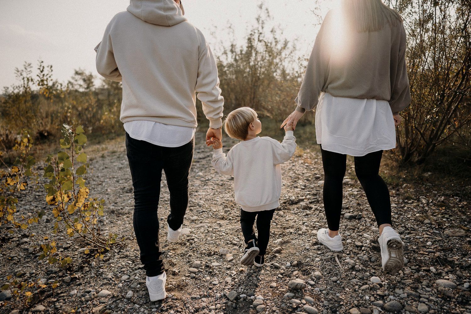 Eine Familie geht Hand in Hand einen Feldweg entlang.