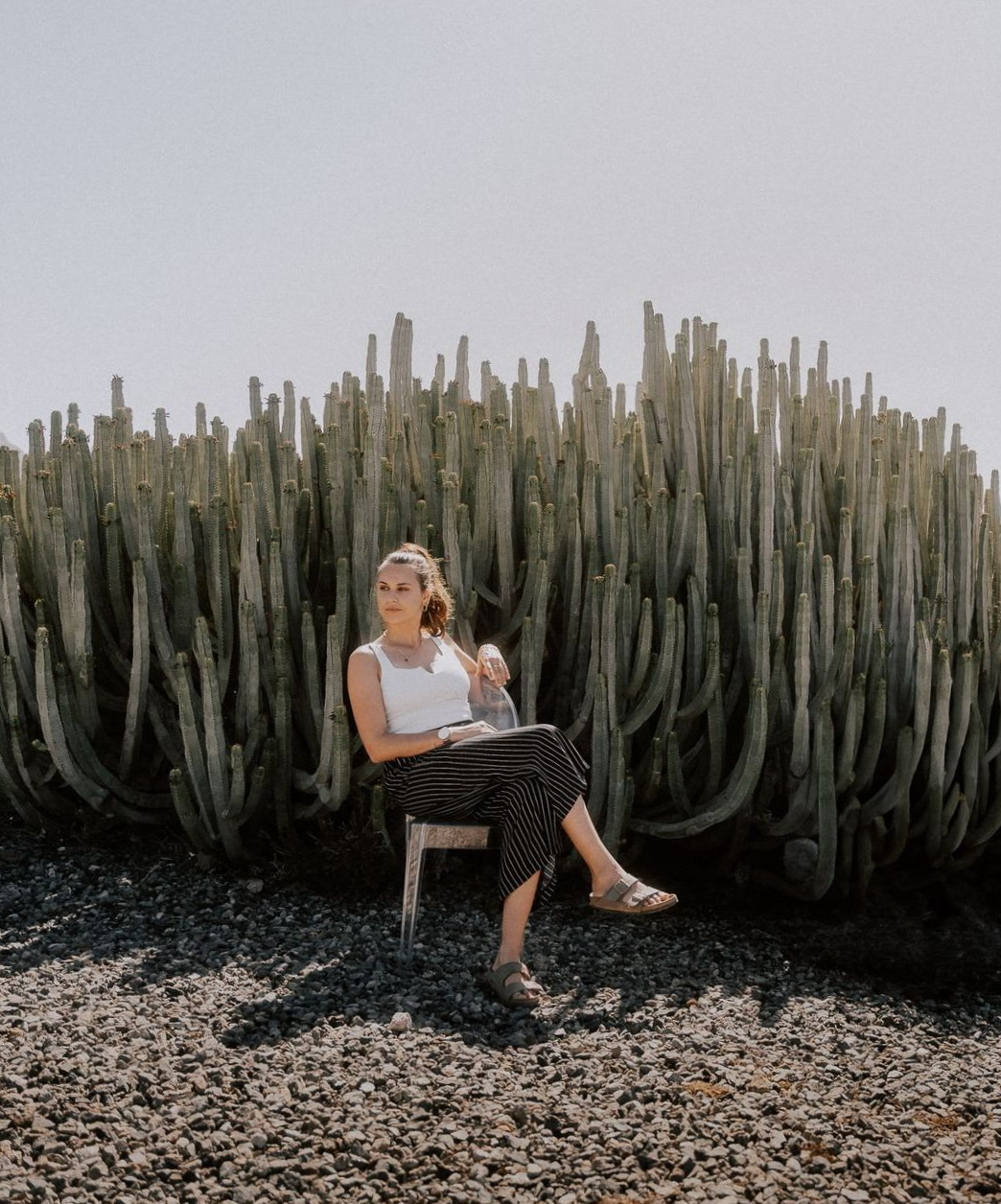 Portrait der Fotografin selbst, wo sie lässig auf einem gläsernen Stuhl vor einen Riesenkaktus sitzt