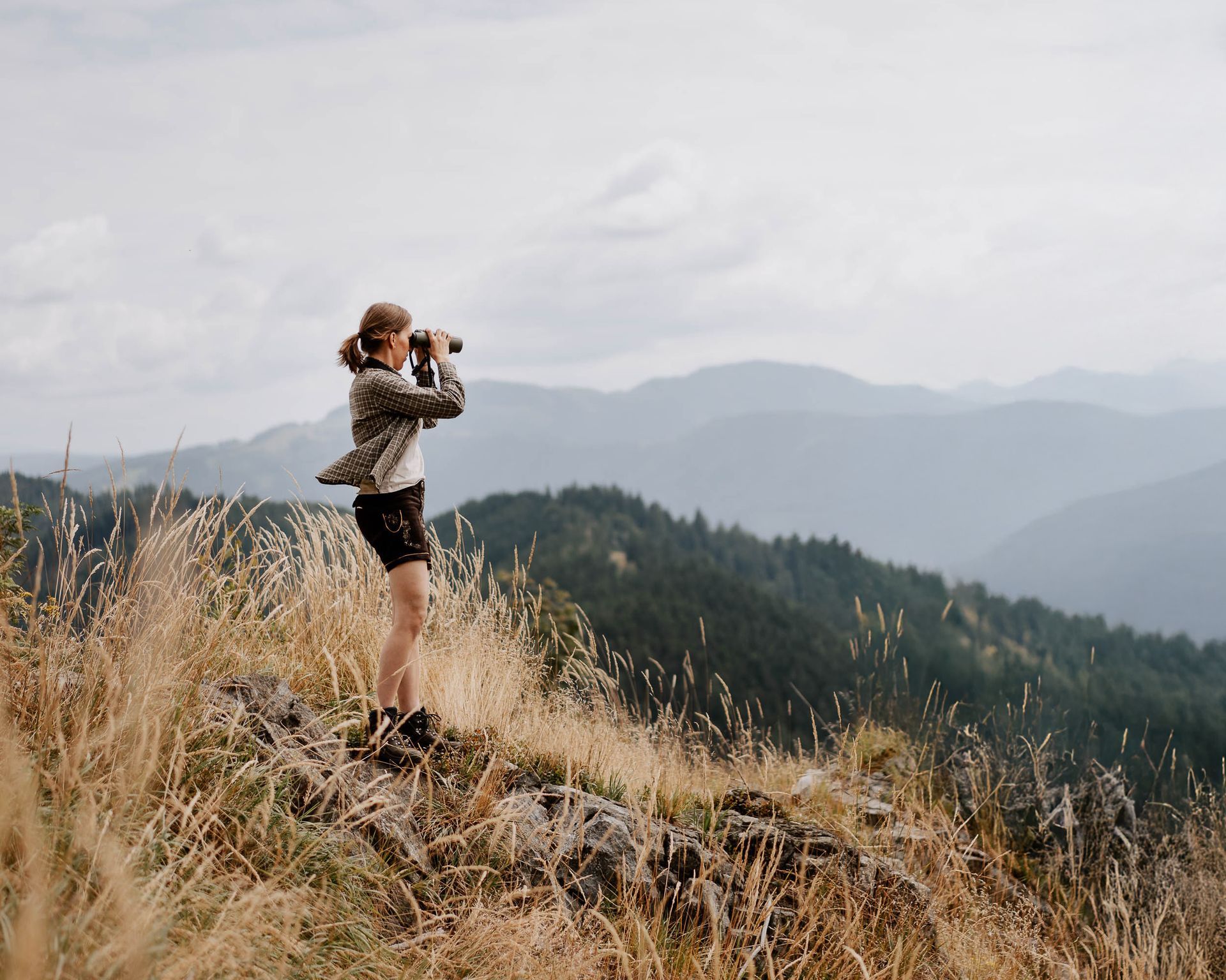 Jägerin sieht mit Fernrohr über weite Landschaft am Berg 