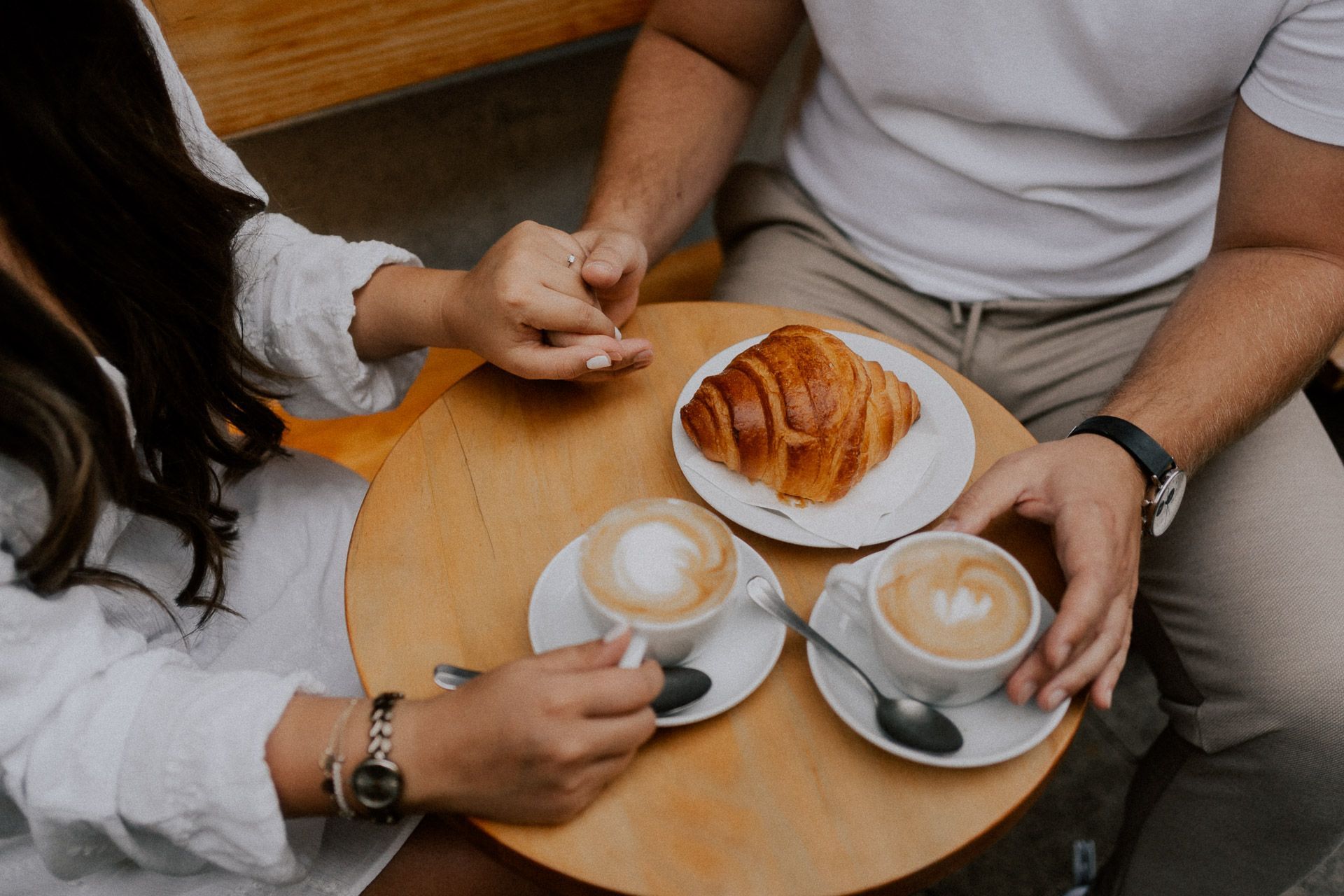 Detailaufnahme von Kaffee, Croissant und Händchenhalten