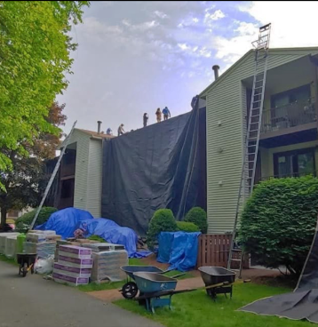 Roofers working on a building with a tarp covering the roof; equipment and supplies on the ground.