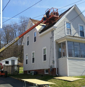 House roof being worked on, aerial lift in use. Construction occurring on a sunny day.
