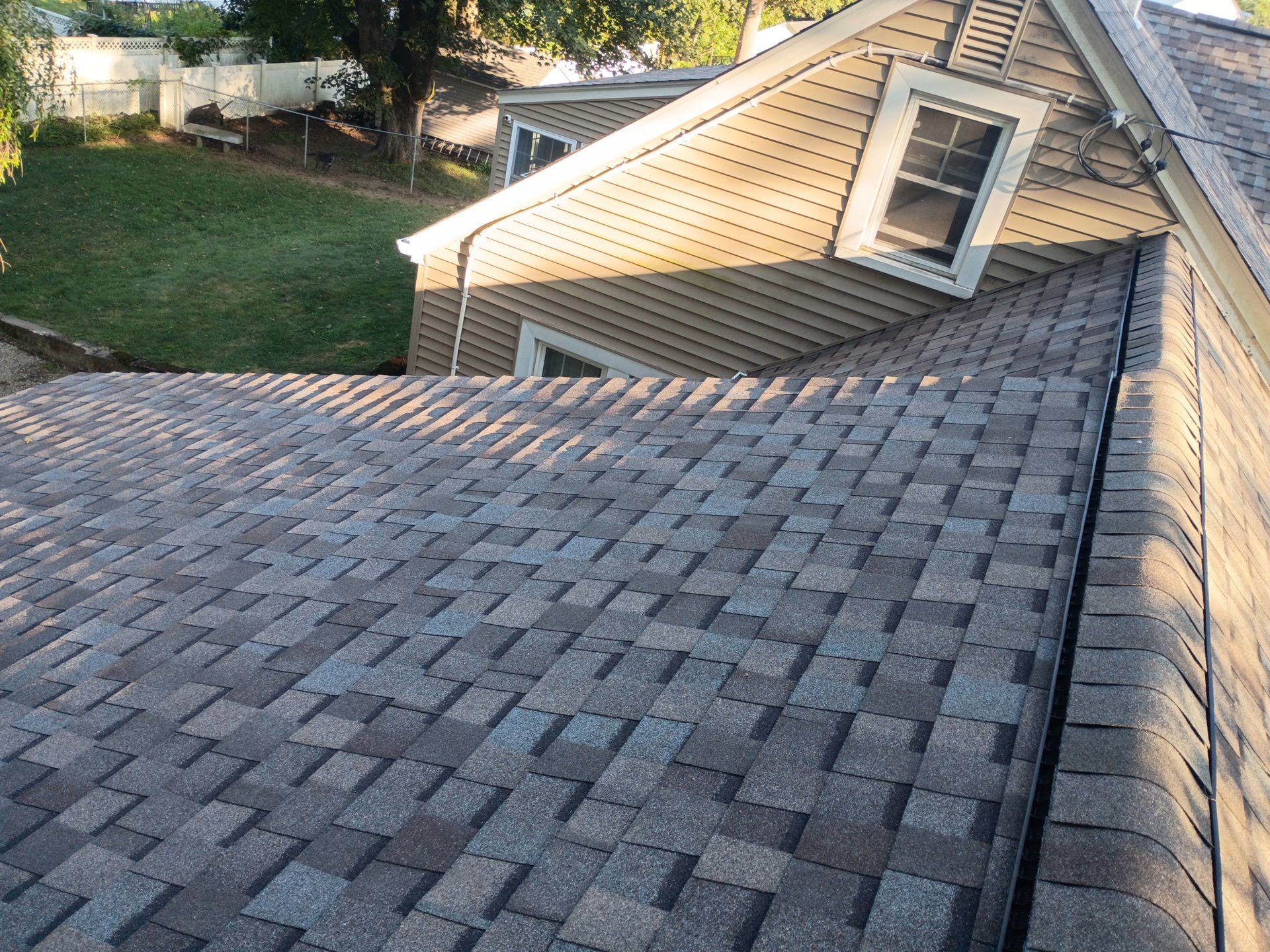 Asphalt shingle roof with varied brown and gray tones. A dormer with a window and siding is visible.