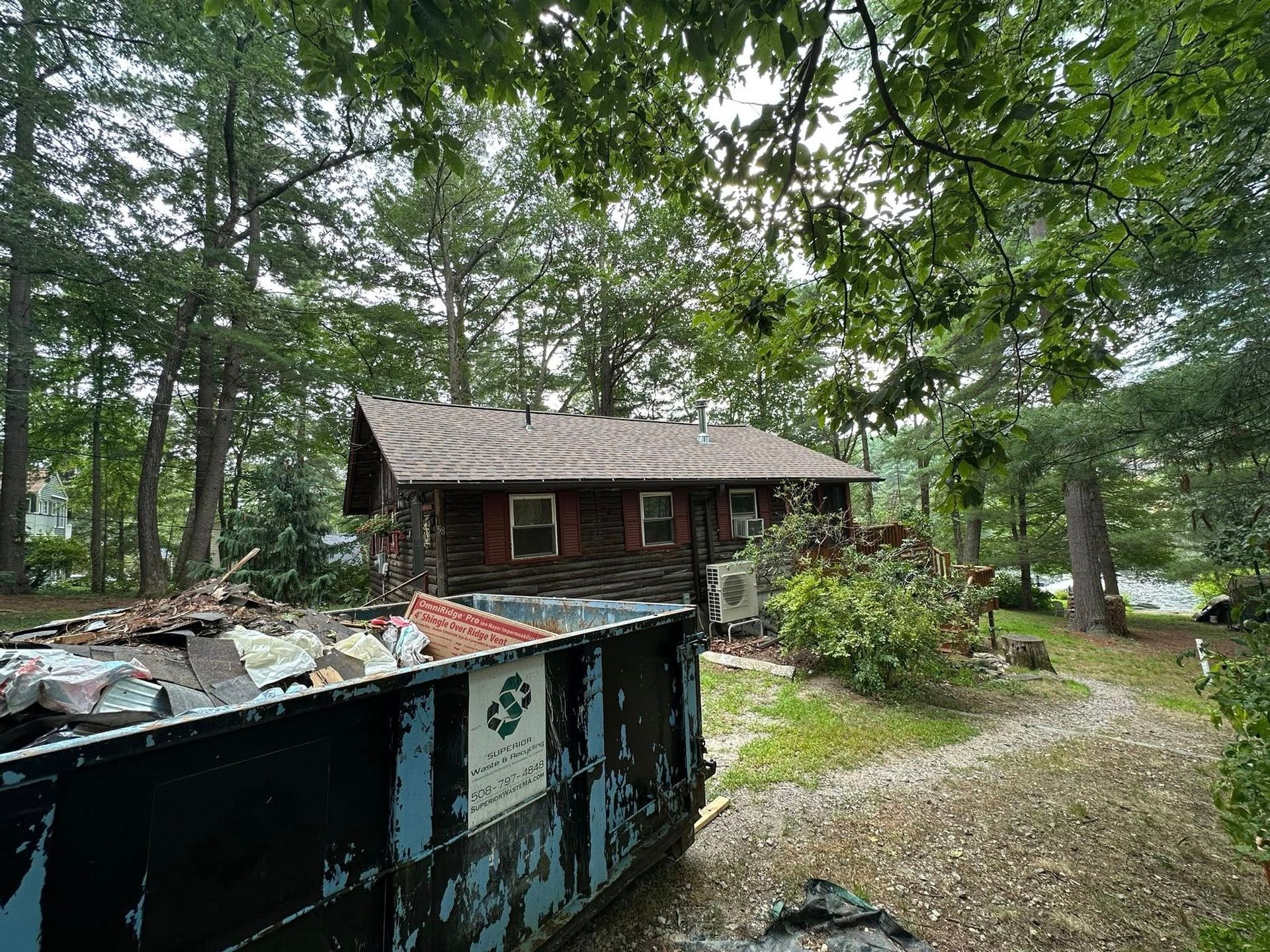 House with debris in front, surrounded by trees, overcast day.