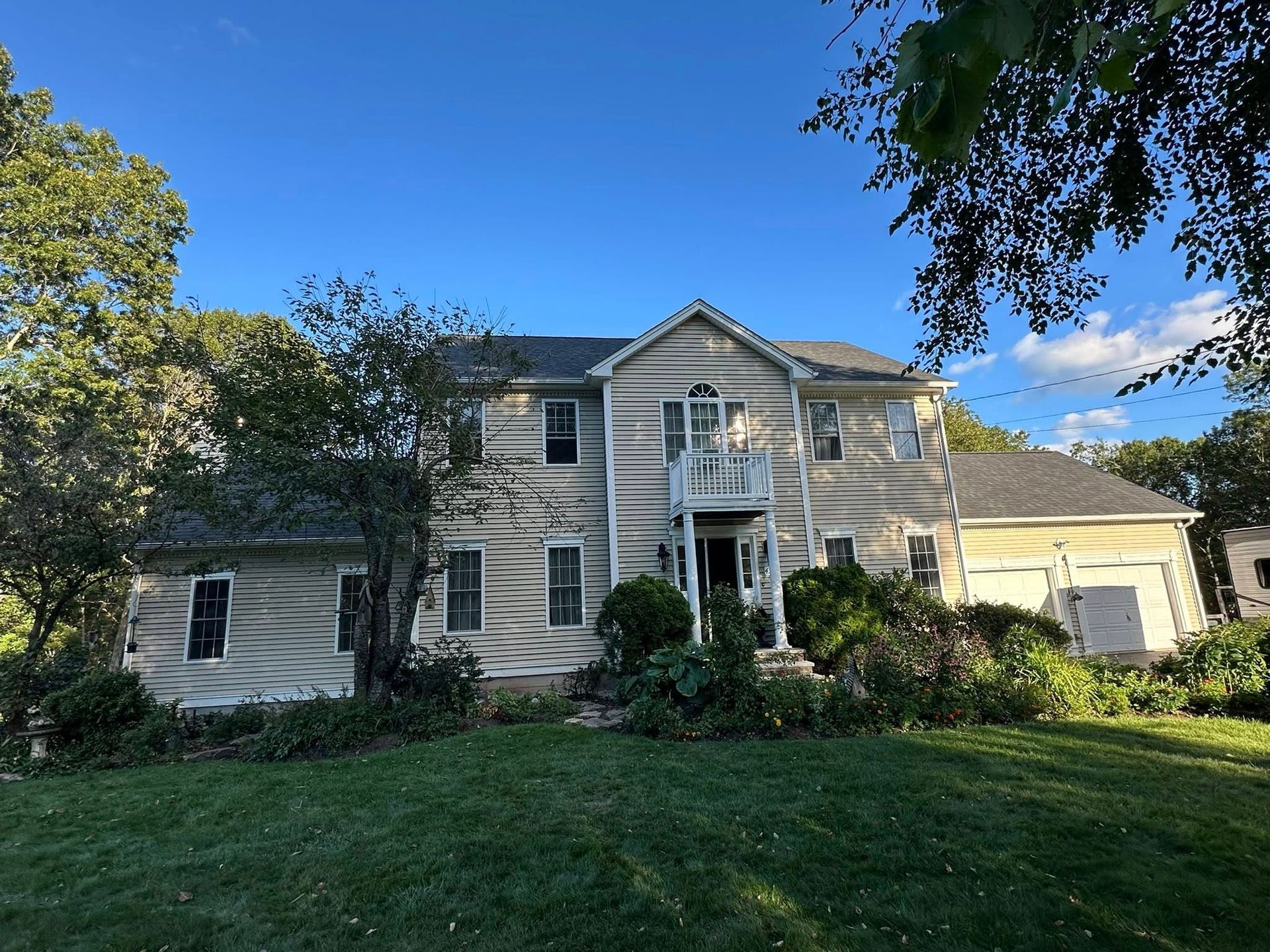 Two-story house with light-colored siding, green lawn, and trees under a blue sky.