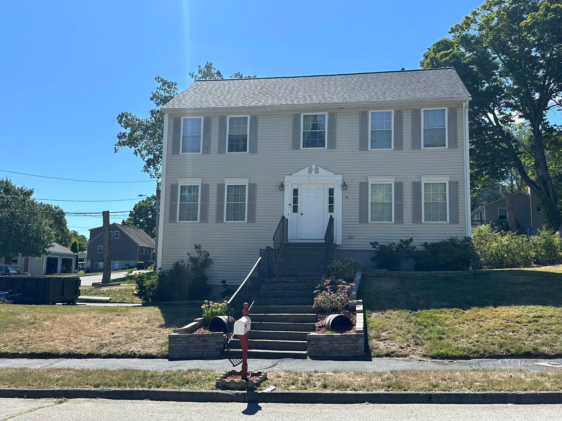 Two-story beige house with shutters, steps leading to the front door, on a sunny day.