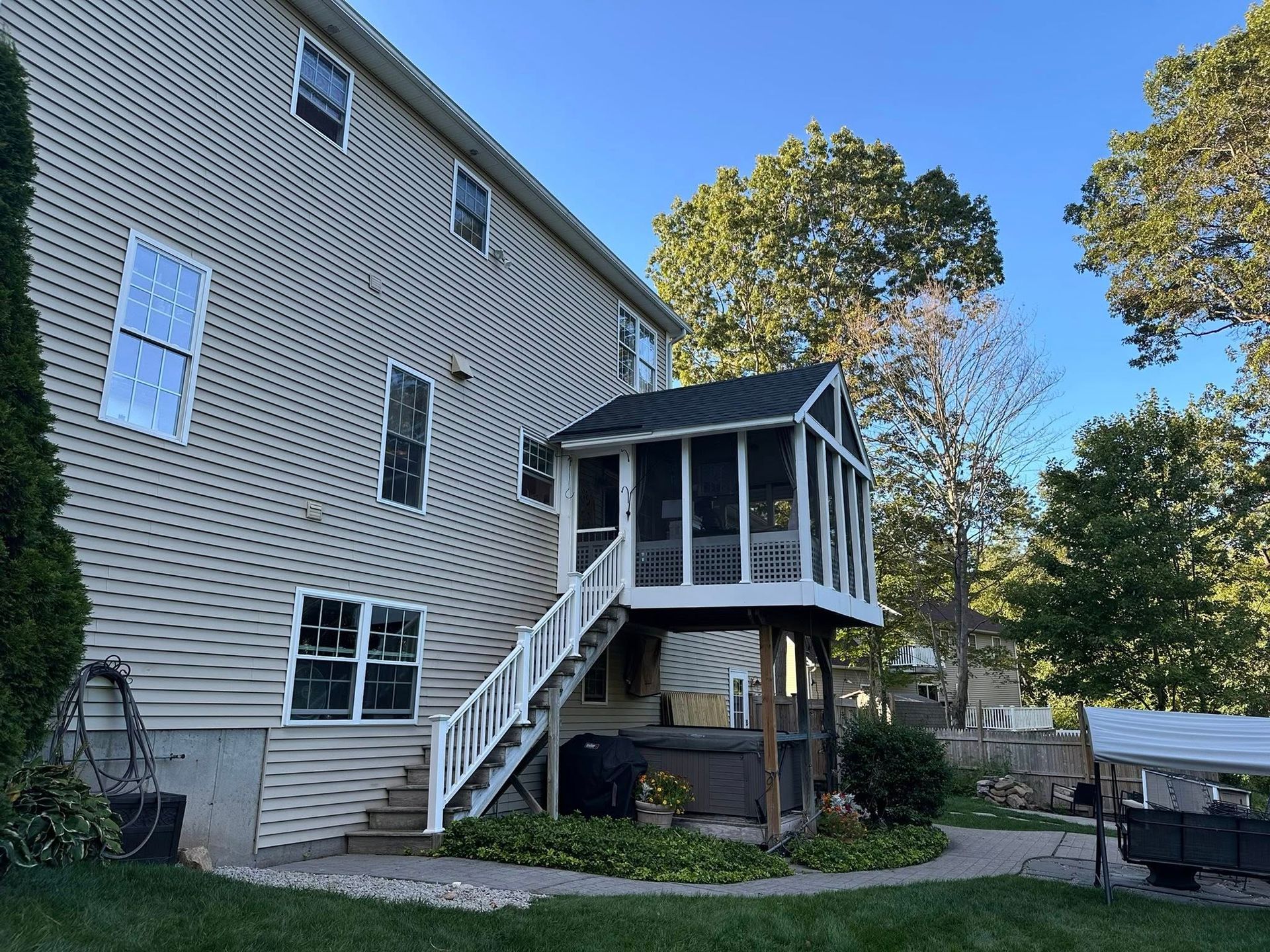 Two-story house with a screened porch, white stairs, and a hot tub, under a blue sky.