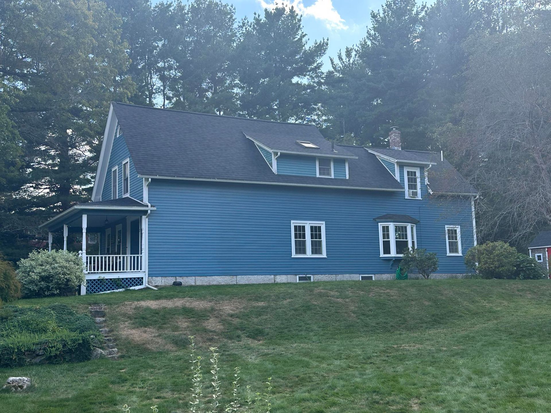 Blue house with white trim and a porch, set against a backdrop of trees and a blue sky.