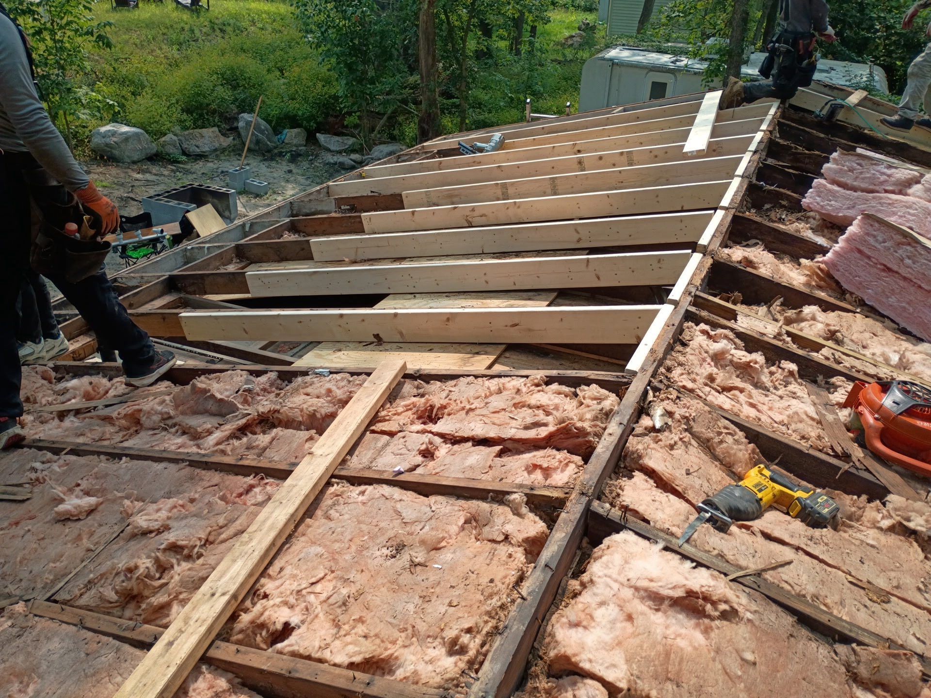 Construction workers repairing a roof; wooden beams and insulation visible. Outdoors on a sunny day.