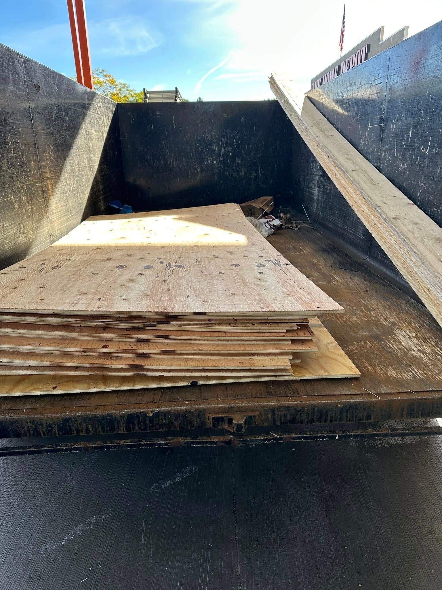 A stack of weathered plywood boards inside a dump truck bed. Blue sky background.