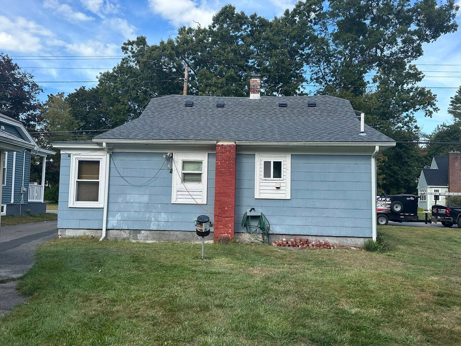 Blue house with gray roof and red brick chimney, green lawn, trees in background.