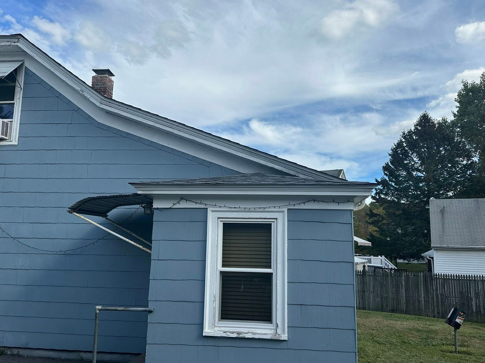 Blue house exterior with a window, roof, and cloudy sky.