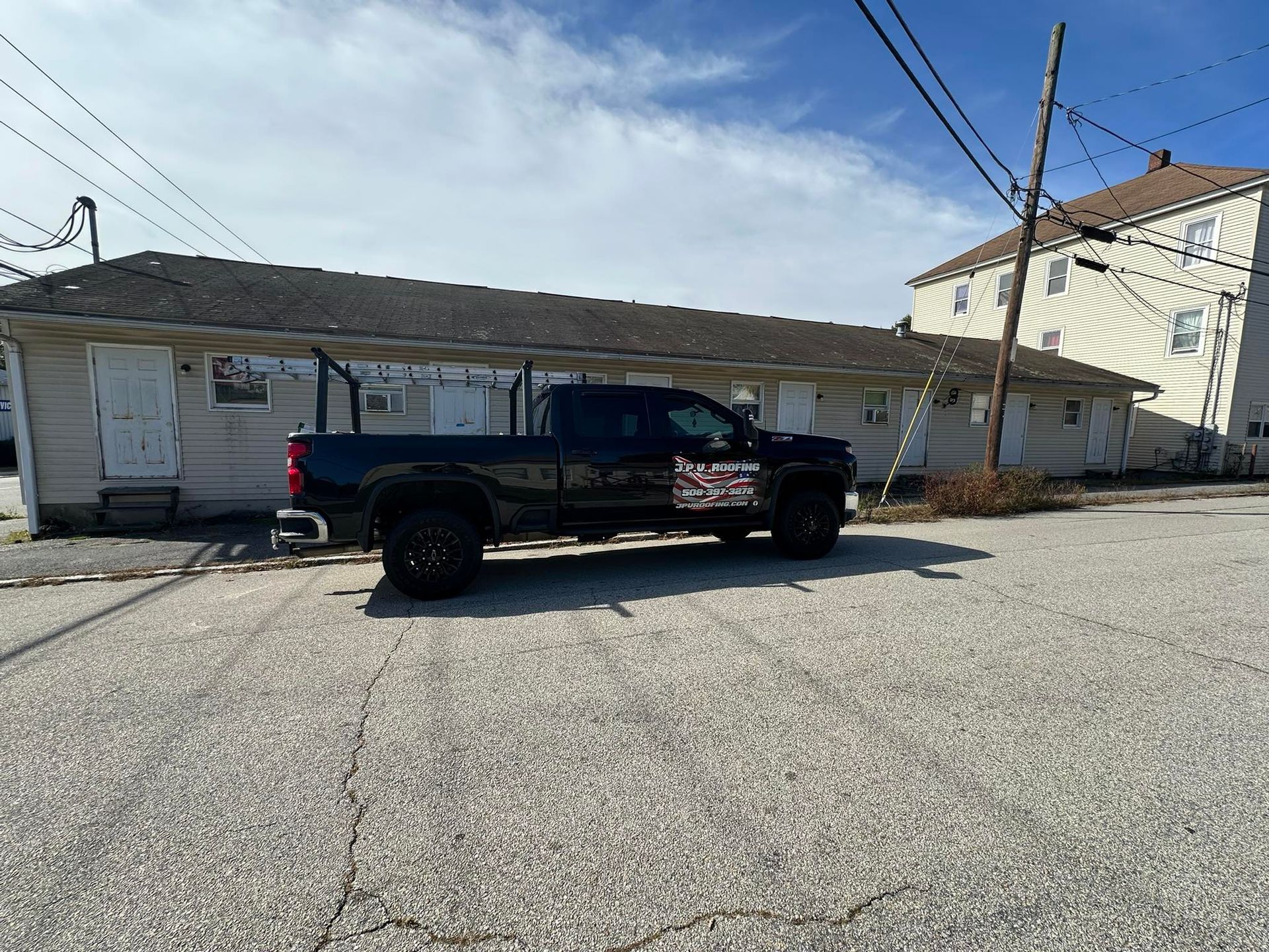 Black pickup truck parked in front of a one-story building with white doors, under a cloudy sky.