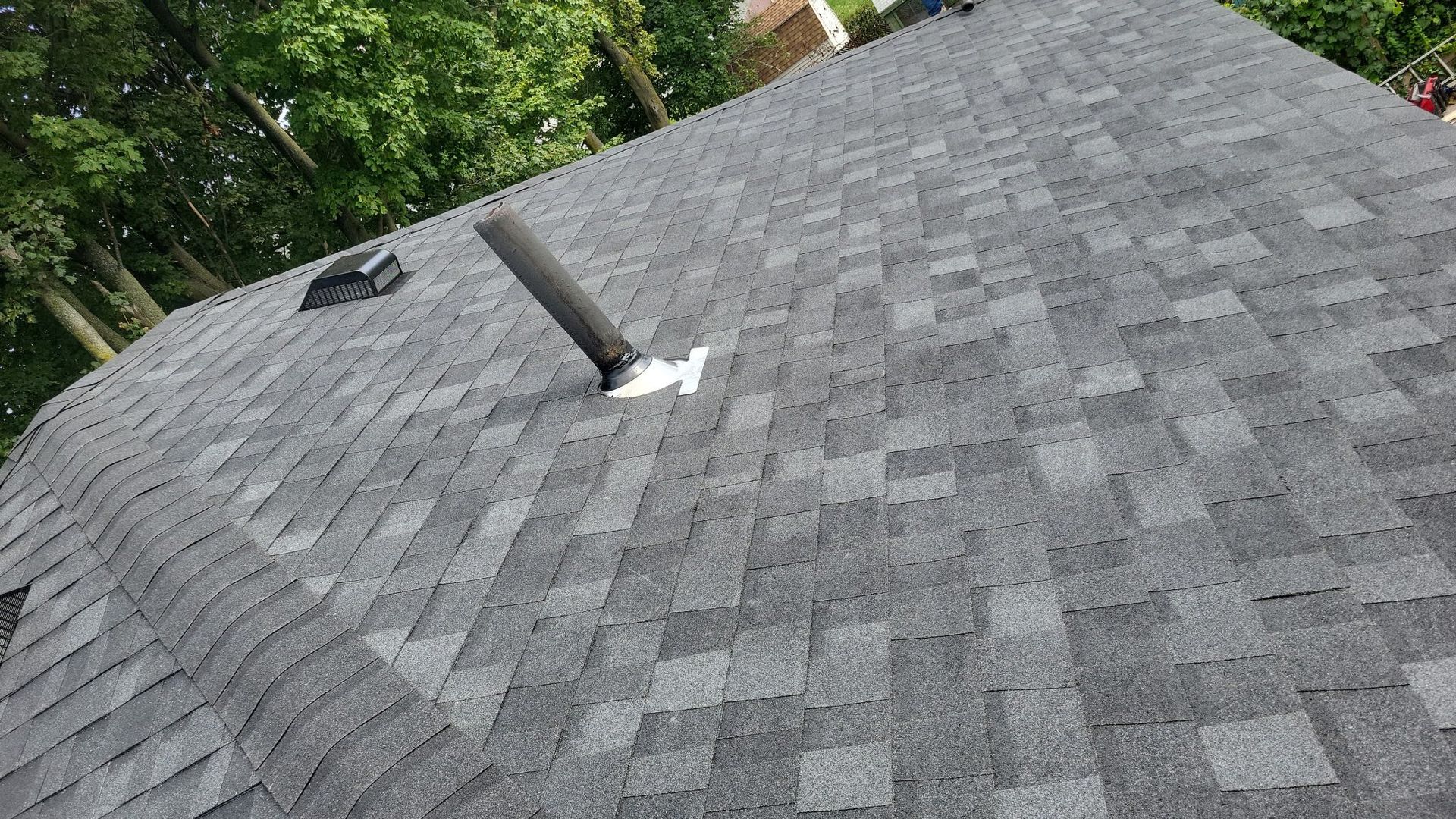 Gray asphalt shingle roof with a vent pipe and a small square vent.