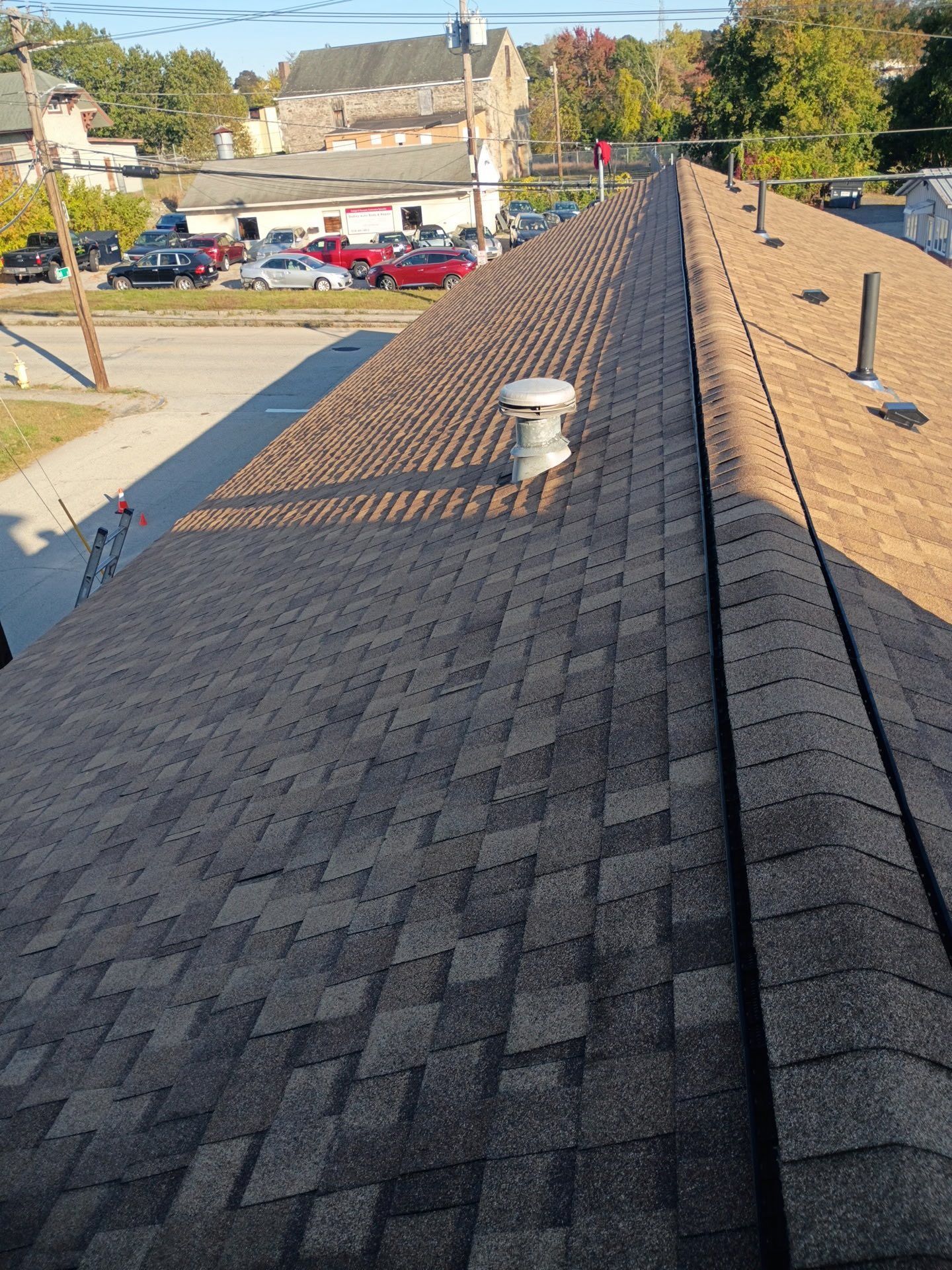 Rooftop with brown shingles and several vents, viewed from above on a sunny day.