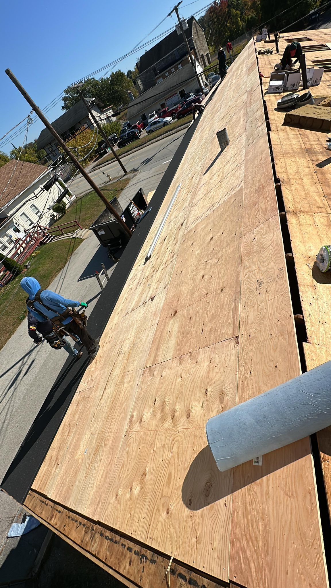 Roofer in blue safety gear on a roof, securing materials. Buildings and street in the background.
