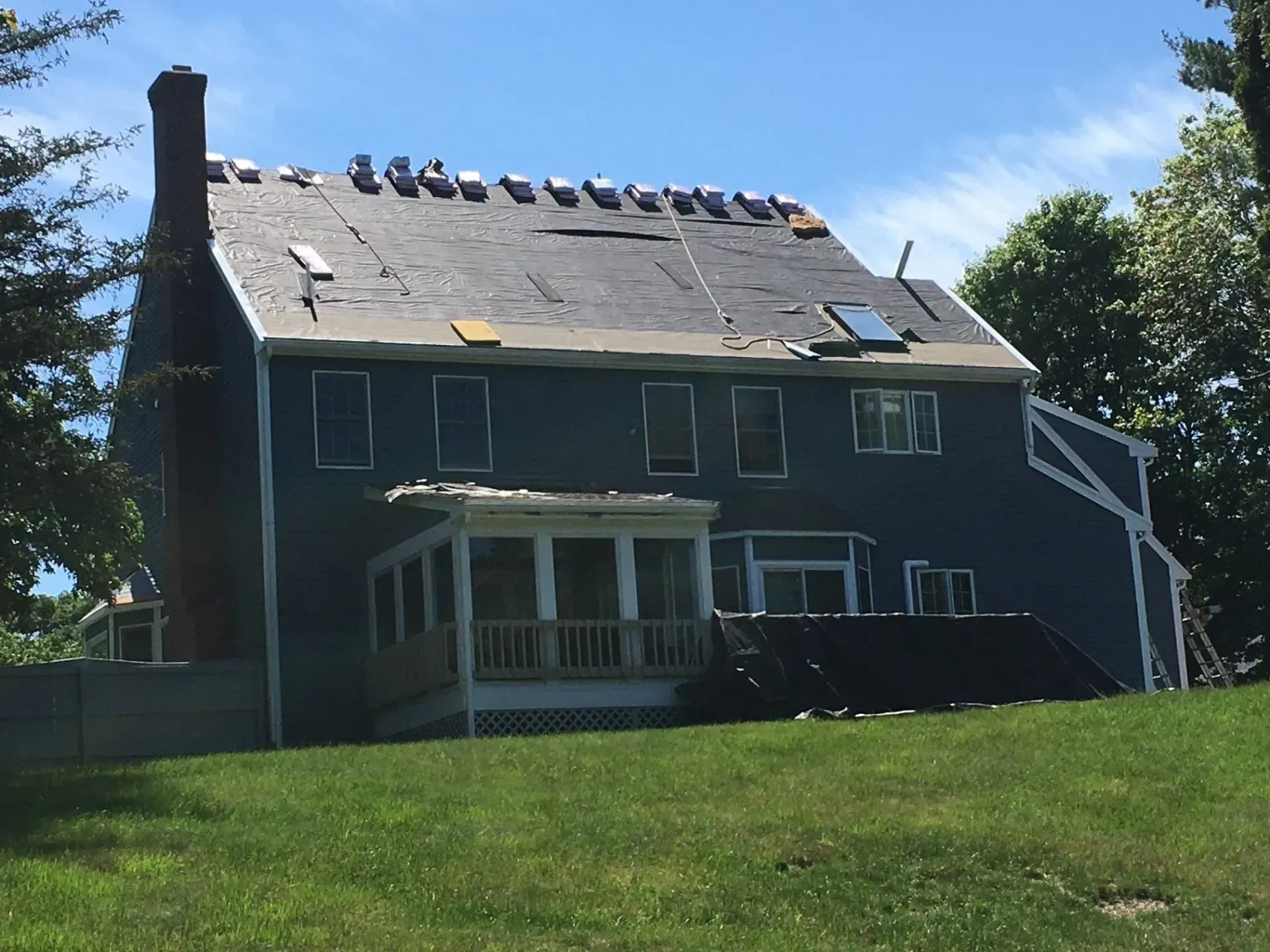 Blue house with partially removed roof; chimney, skylights, sunny day.
