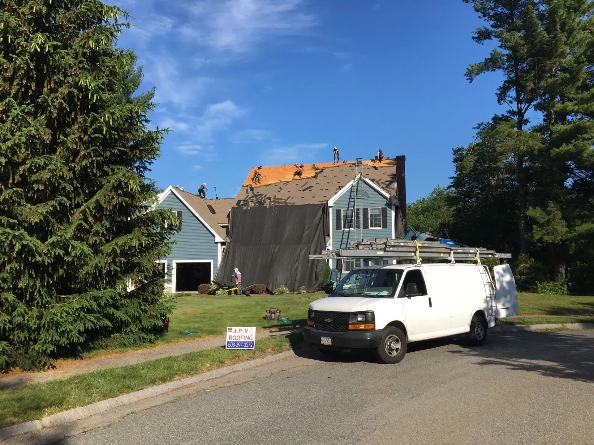 House under construction with roof partially removed, white van parked on street.