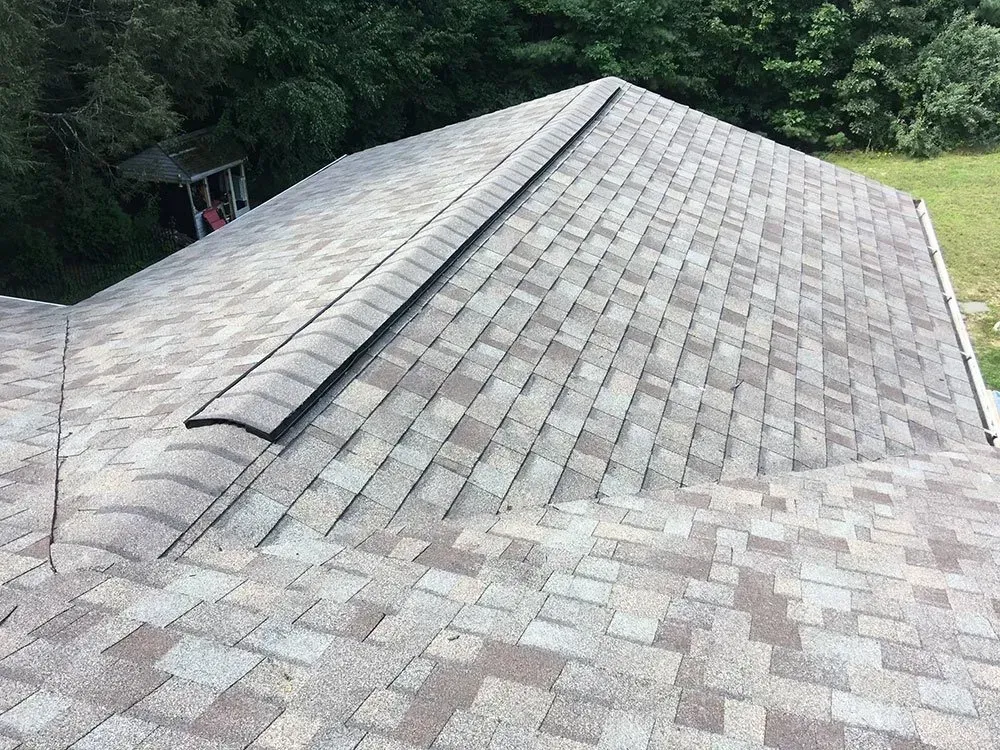 Gray and brown asphalt shingle roof with ridge vent, set in a yard.