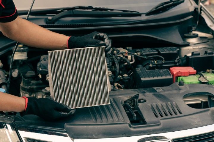 A person is holding a filter in front of a car engine.