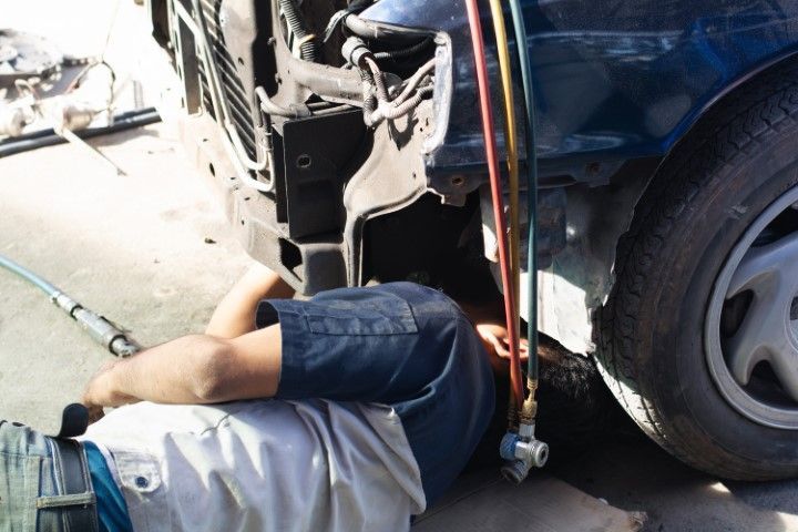 A man is laying on the ground working on a car