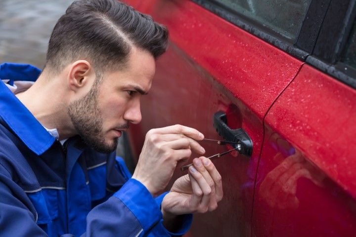 A man is trying to open a car door with a screwdriver.