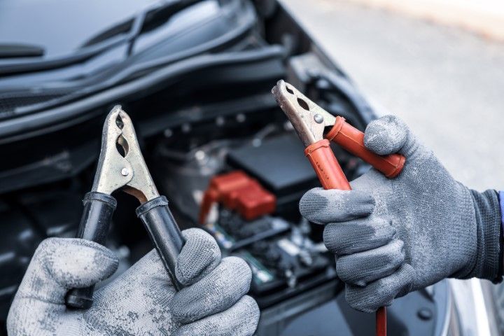 A person is holding a pair of jumper cables in front of a car.