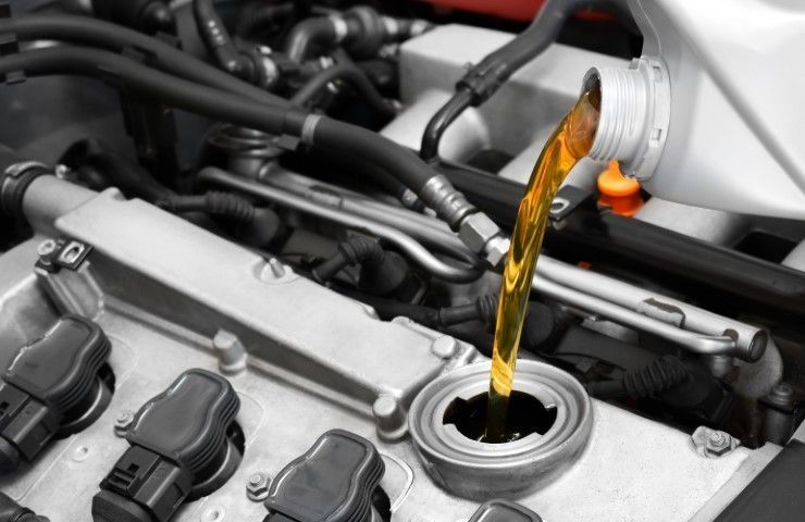 A close up of a car engine with oil being poured into it