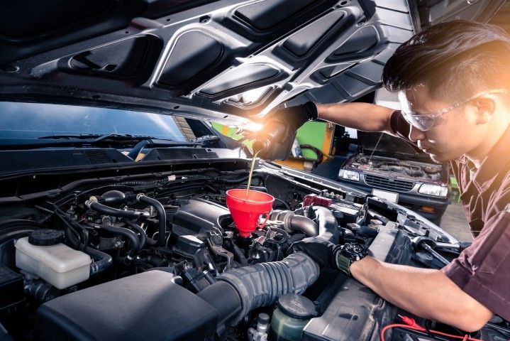 A man is pouring oil into a car engine.