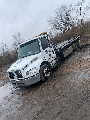 A white tow truck is parked on the side of a dirt road.