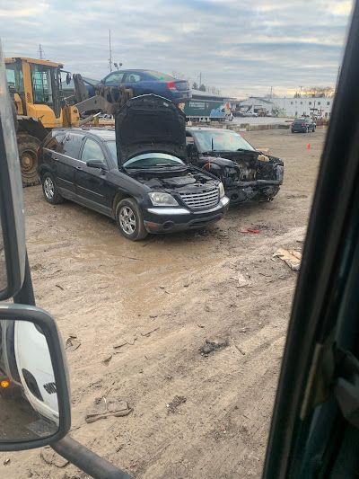 A black car with its hood up is parked in a dirt lot.