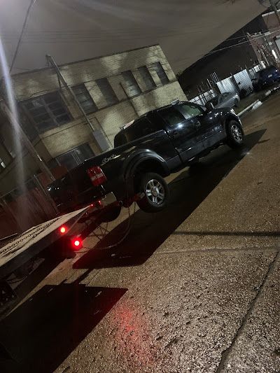 A black truck is parked on the side of the road next to a tow truck.