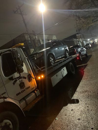 A tow truck is towing a car down a street at night.