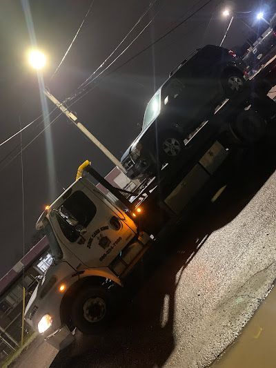 A tow truck is towing a black car at night.