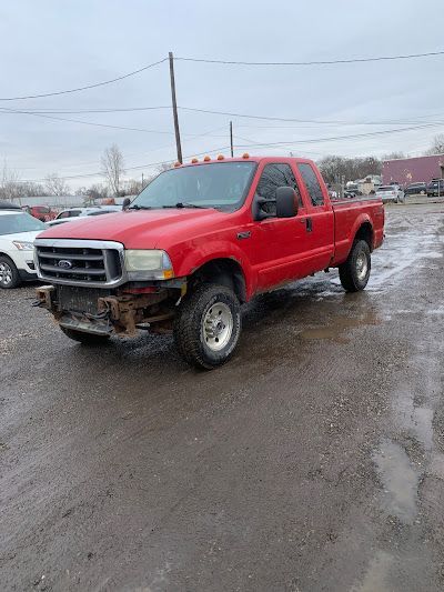 A red ford f250 pickup truck is parked in a muddy parking lot.