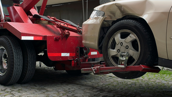 A tow truck is towing a car with a damaged front end.