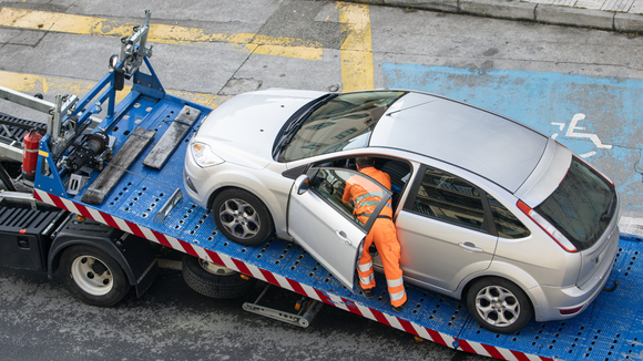 A man is standing next to a tow truck with a car on it.