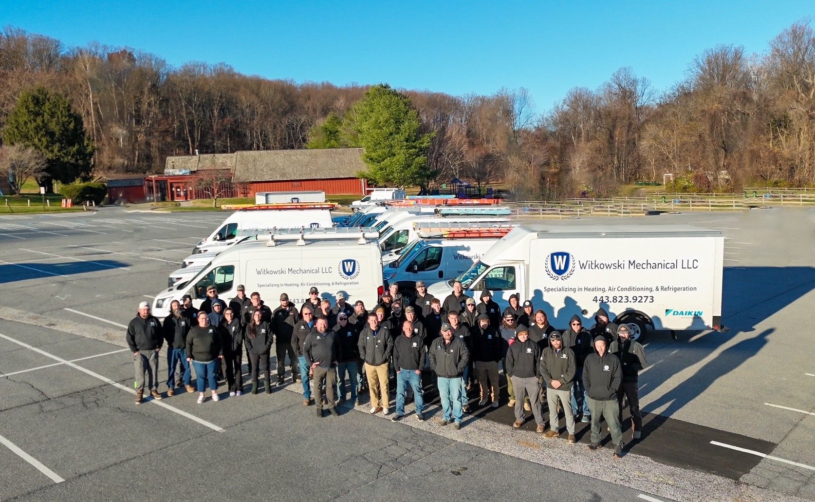 A group of service workers stand in front of their white vans. They are in blue company shirts.