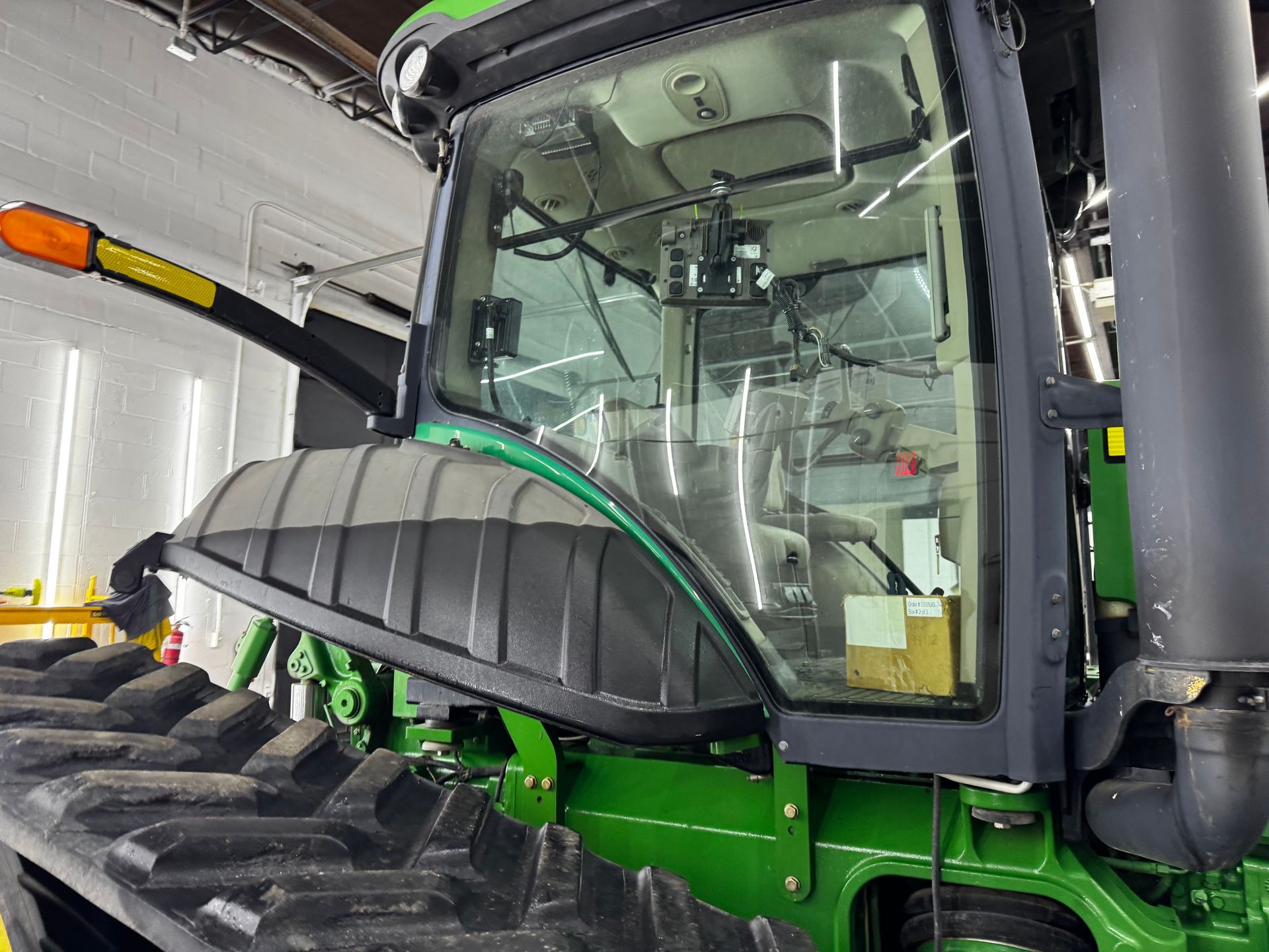 Green and black combine harvester cab with large front tire inside a workshop