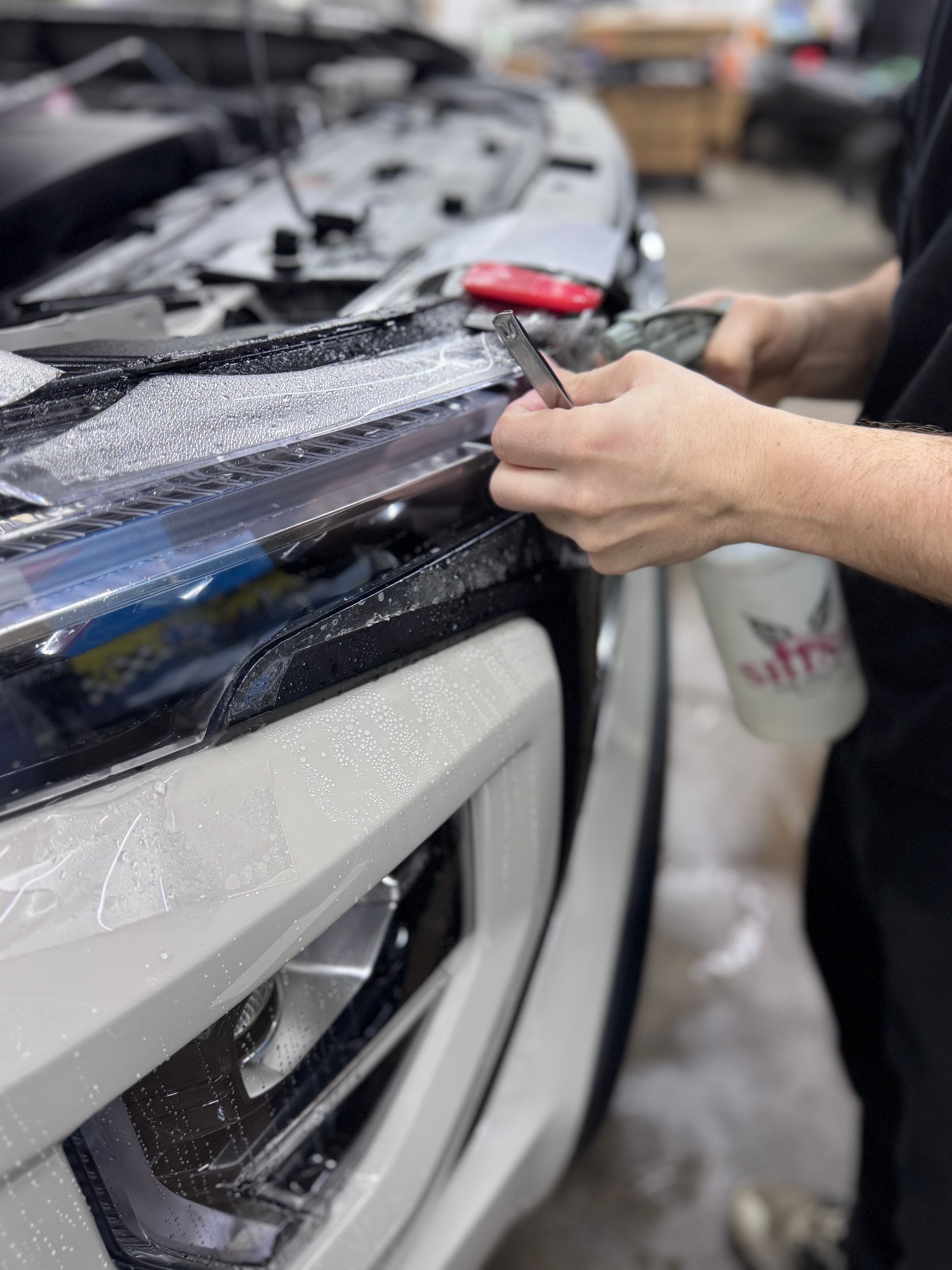 Car detailer applying protective film to a car headlight and front bumper with a red squeegee