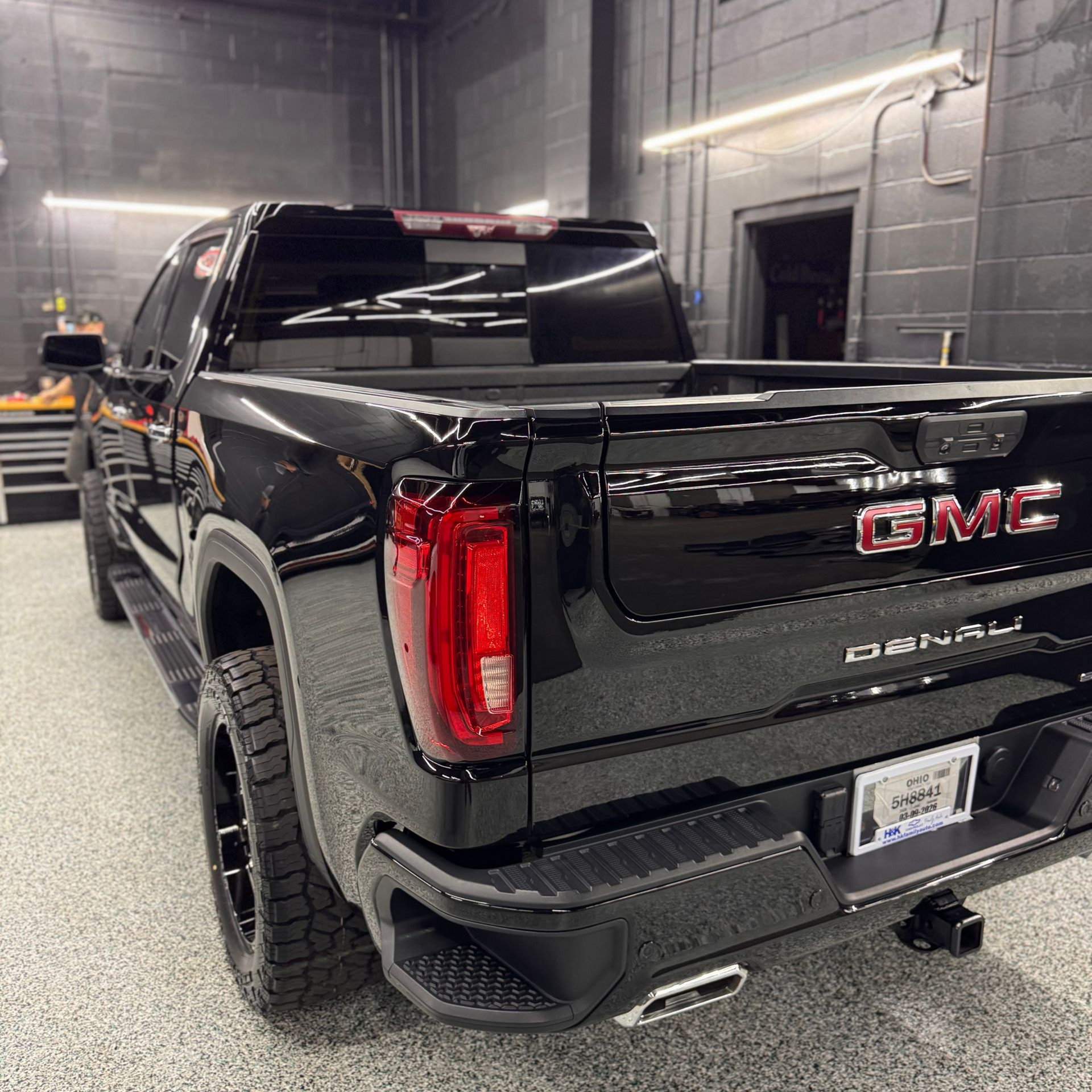 Black GMC Canyon pickup truck parked indoors in a garage, rear three-quarter view