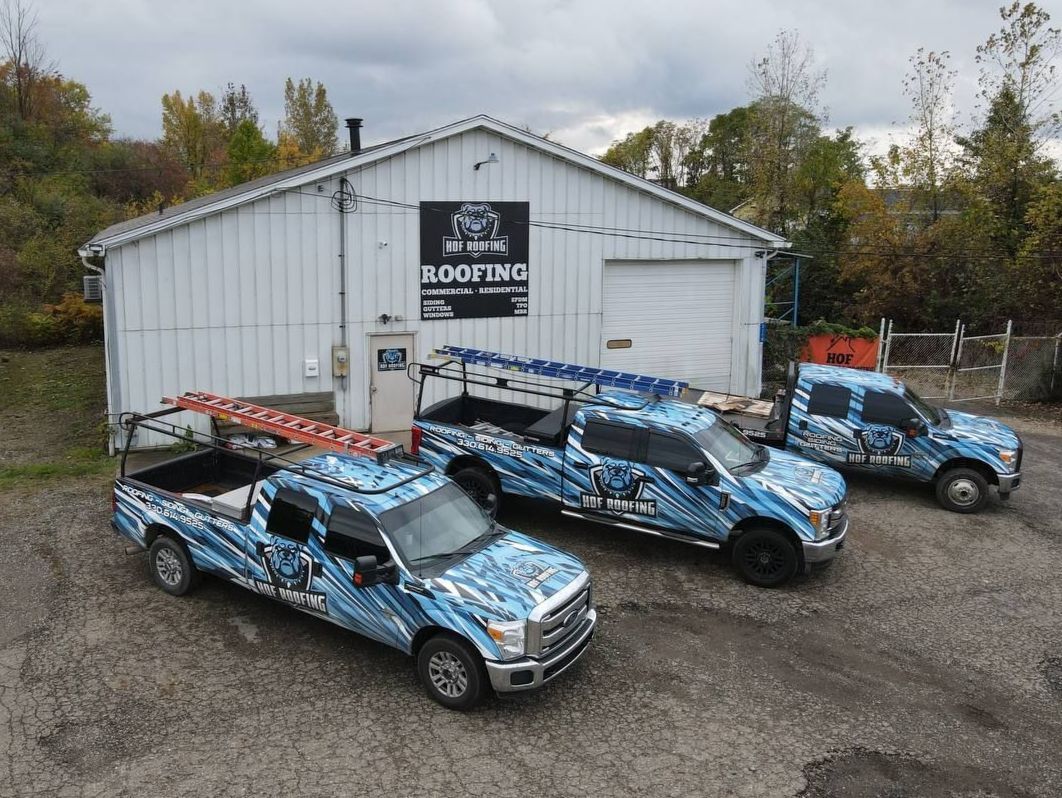 Three trucks are parked in front of a building that says roofing