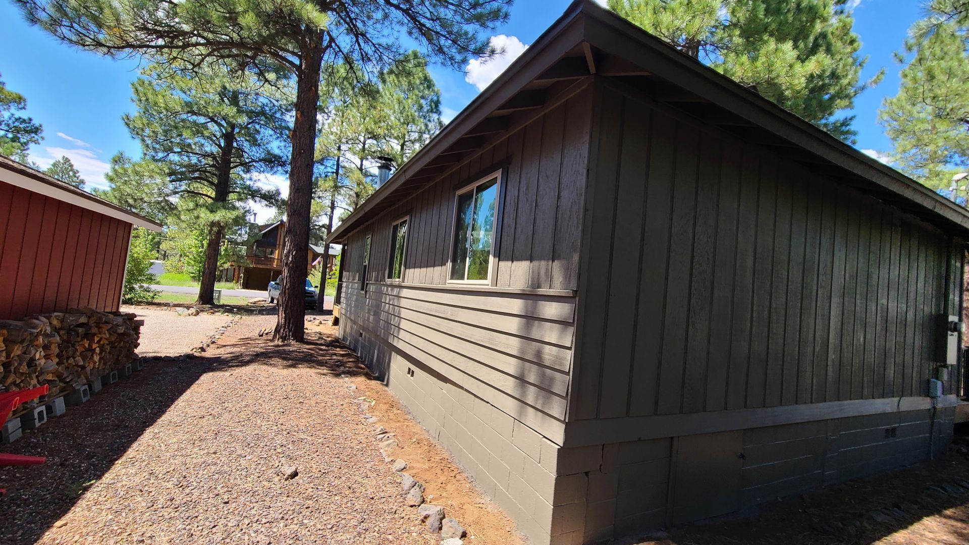 Brown wooden cabin exterior with gravel ground, trees, and blue sky.