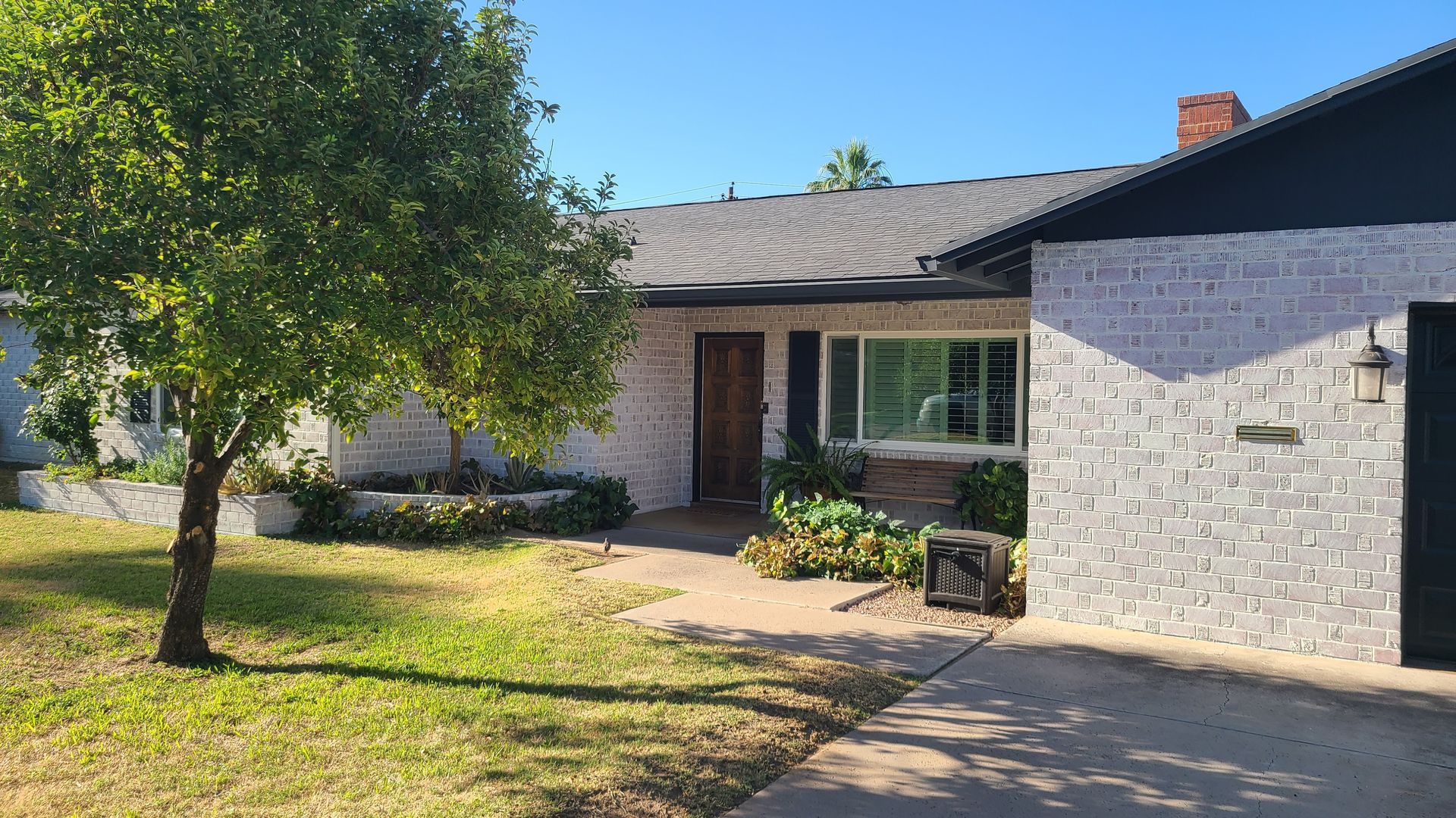 A single-story house with light-colored brick facade, a small tree in the front yard, and a driveway.