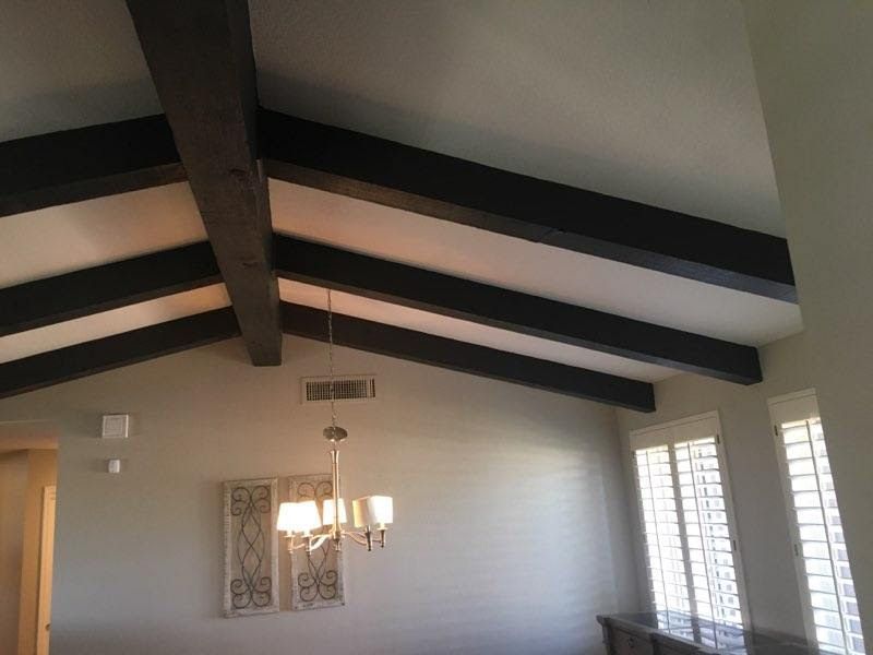 Angled ceiling with dark brown beams, chandelier, and windows. Interior view.