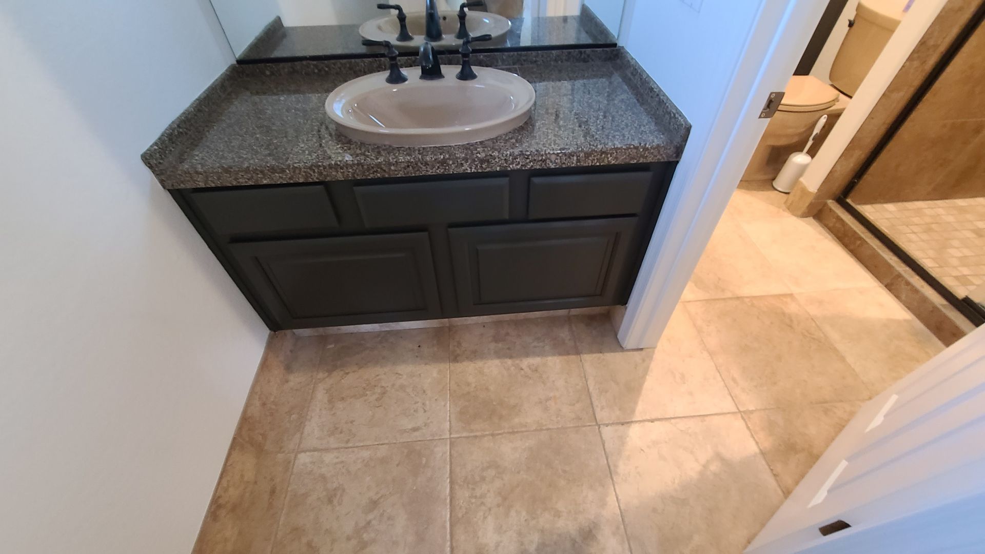 Bathroom vanity with dark gray cabinets, speckled countertop, and beige tiled floor.